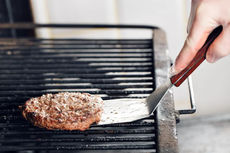 beef burgers and spatula on the hot flaming bbq charcoal grill, close-up