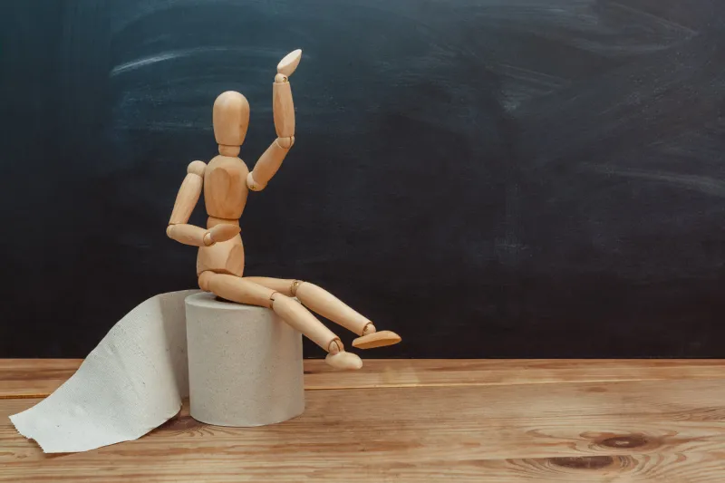 wooden figure sit on a roll of toilet paper concept of the problem with digestion