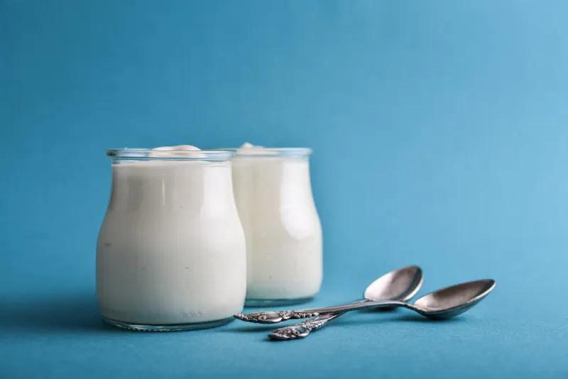 greek yogurt in a glass jars with spoons on blue background closeup