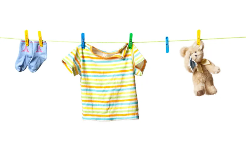 baby clothes and a teddy bear drying on a rope isolated on white background
