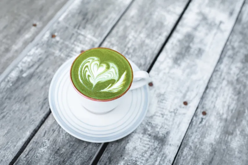 cup of fresh green matcha latte beverage with latte art on foam background of wooden table with gray shabby aged surface view from above healthy drink