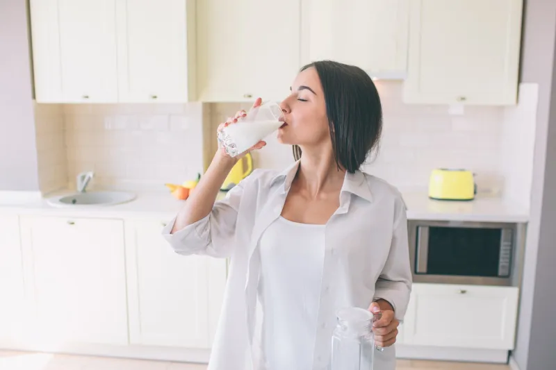 attractive and amazing girl stands in kitchen at table and drinking milk she is keeping her eyes closed girl enjoyes the moment