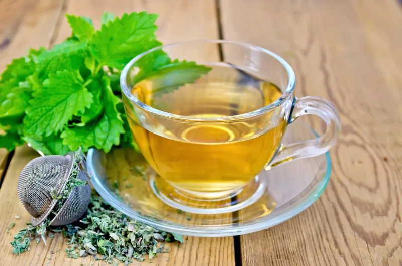 herbal tea in a glass cup, metal sieve with dry mint leaves, fresh mint leaves on the background of wooden boards