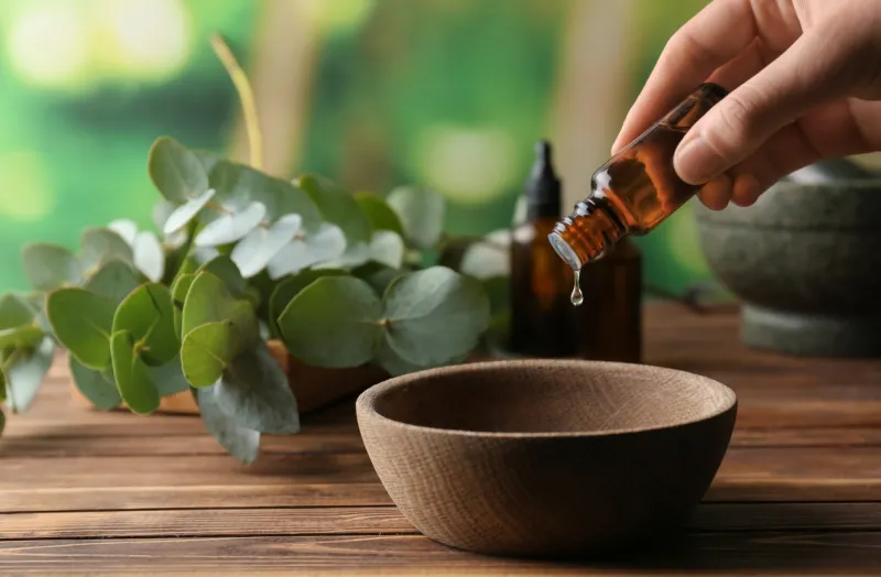 woman pouring eucalyptus essential oil into bowl on wooden table