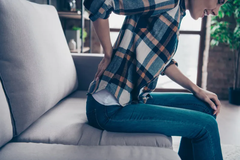 cropped close up side profile photo beautiful she her lady arms hands hold, back spine suffering terrible pain wear jeans denim checkered plaid shirt sit divan comfort flat house living room indoors