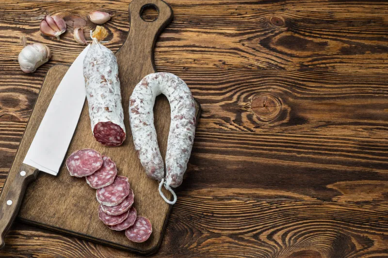 traditional sausage and sausage with mold sliced sausage salami and knife on wooden board with garlic close-up top view
