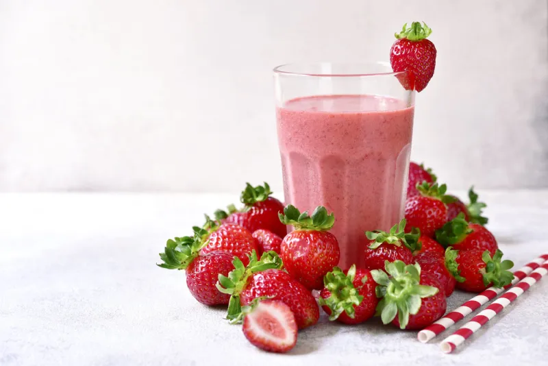 strawberry banana smoothie in a tall glass on a light slate, stone or concrete background