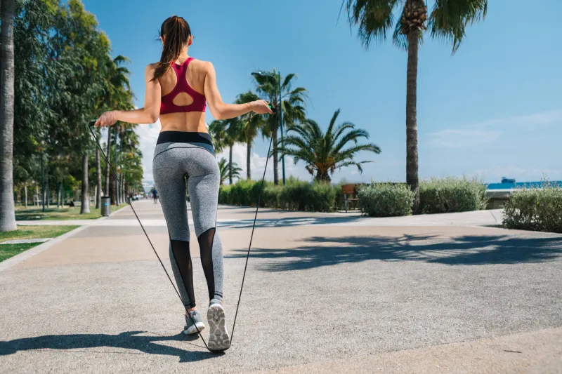sporty young woman is jumping on skipping rope on the seafront focus on back copy space