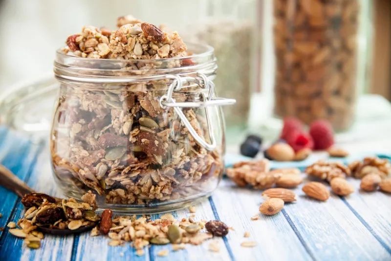 a glass jar in a blue wooden table overfilled with granola