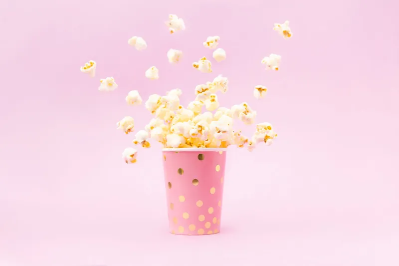 flying popcorn in a bright glass and on a pink background copy space