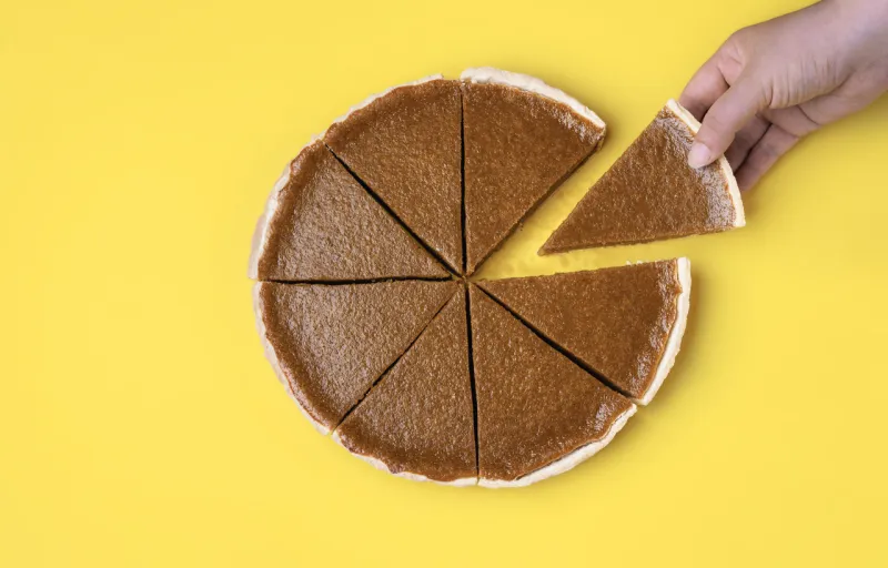 woman hand holding and taking a piece of pumpkin pie on a yellow background above view of traditional autumn dessert thanksgiving sweet food eating pie