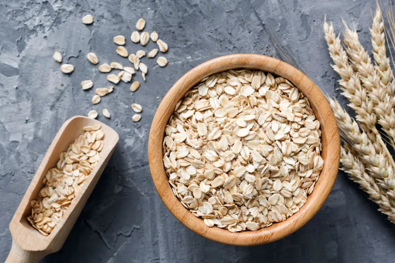 rolled oats or oat flakes in wooden bowl and golden wheat ears on stone background top view, horizontal healthy lifestyle, healthy eating, vegan food concept