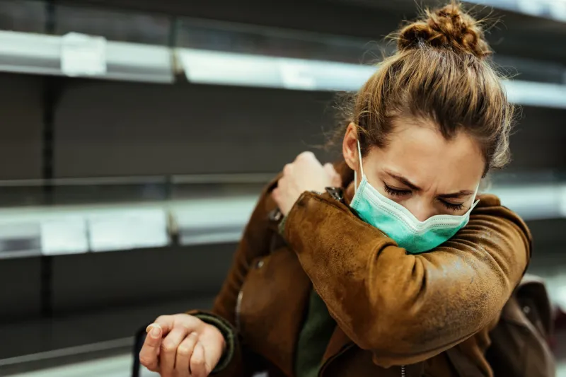 sick woman buying in supermarket and coughing into elbow during covid-19 pandemic