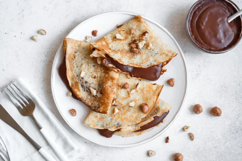 crepes with chocolate spread and hazelnuts homemade thin crepes for breakfast or dessert on white background, copy space