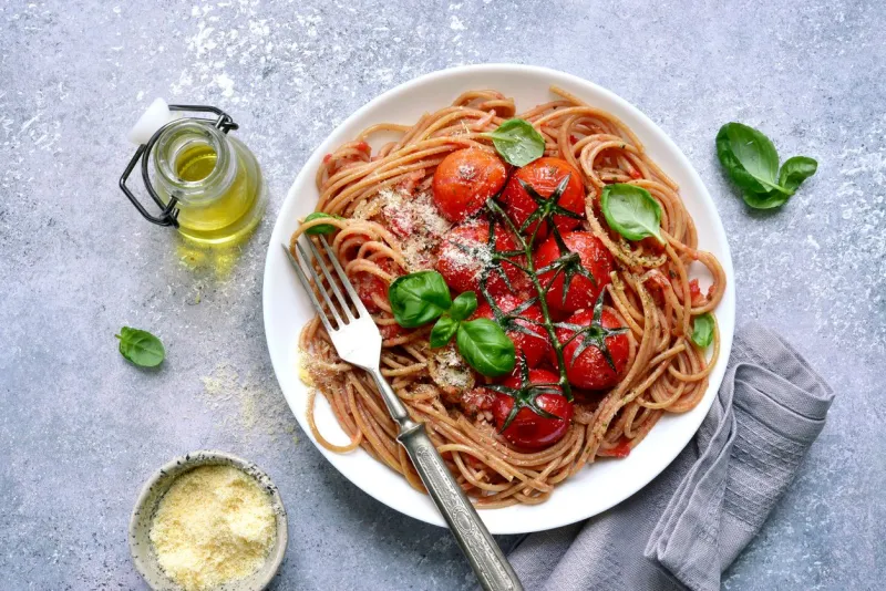 whole grain spaghetti pasta with grilled cherry tomato in a white bowl over light grey slate, stone or concrete backgroundtop view with copy space