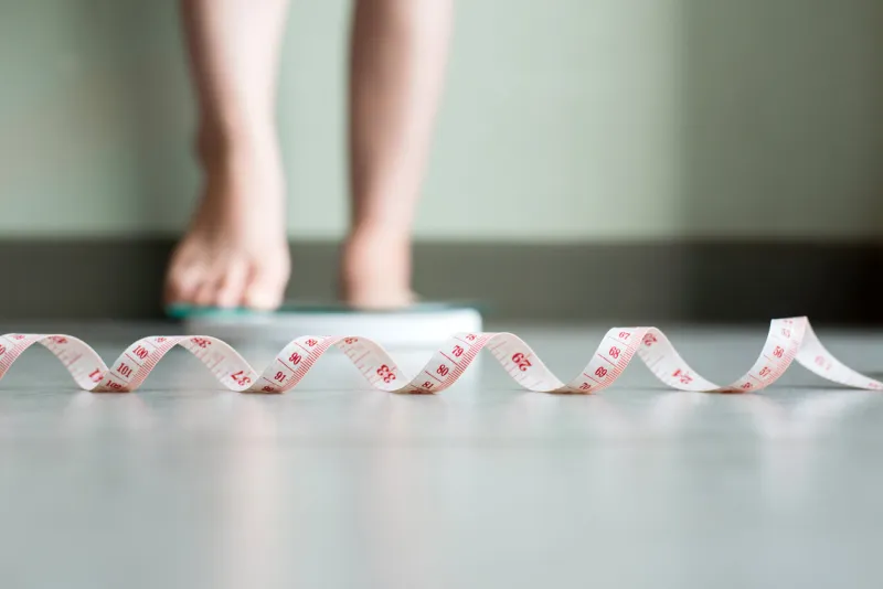 blured of women foot standing on weigh scales with tape measure in foreground
