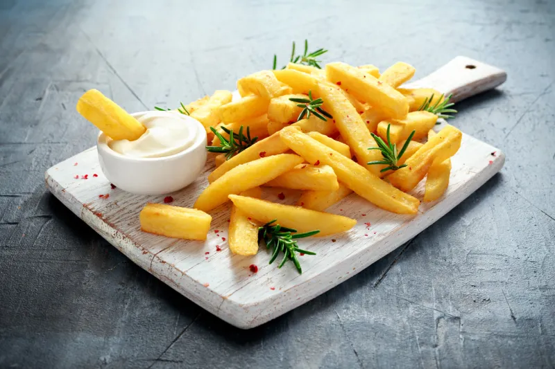 homemade baked potato fries with mayonnaise and rosemary on white wooden board