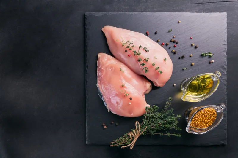 raw chicken fillets on black cutting board with spices and herbs cooking ingredients natural healthy food concept flat lay with space for text
