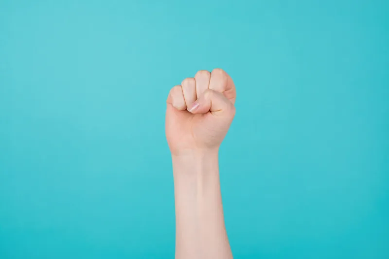 girl power concept cropped photo of woman holding raising up a fist as a sign of triumph isolated on teal turquoise background