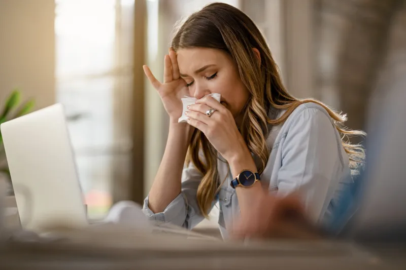 young businesswoman with clpd and flu virus blowing nose while working in the office
