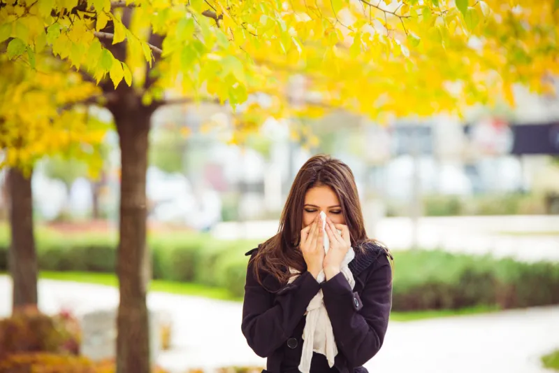 young girl in autumn park blowing nose standing in park in warm clothing