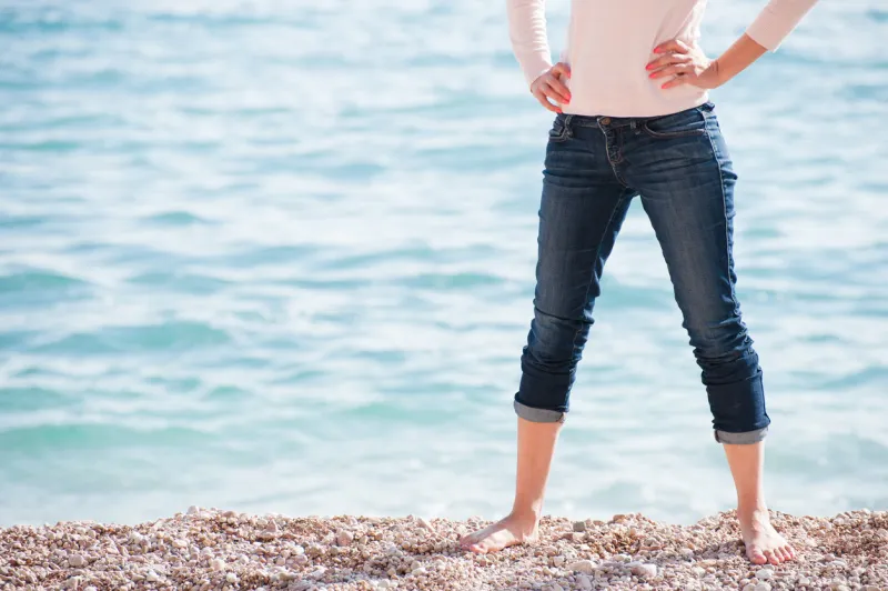 legs of sport young caucasian woman wearing jeans on sea shore background with copyspace