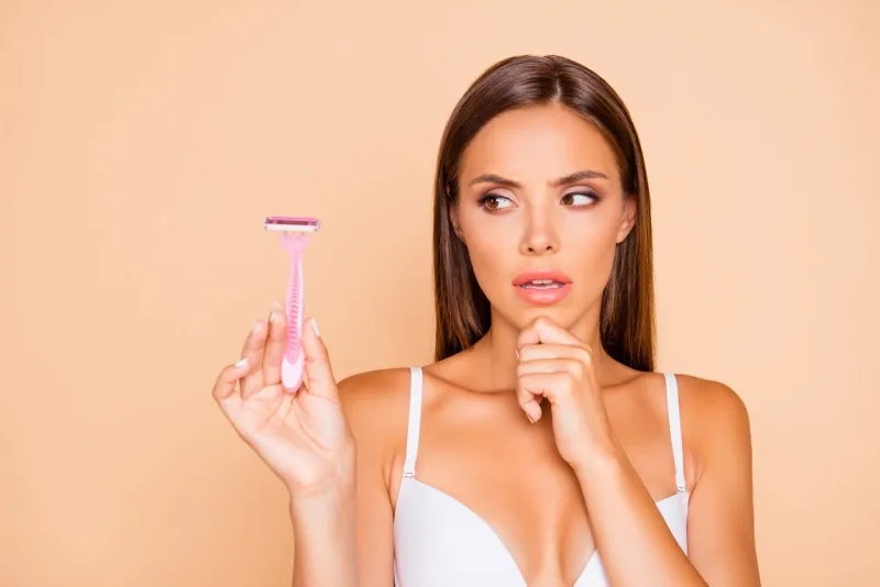 wax or shave close up portrait of thinking lady look aside on safety razor she isolated on pastel beige background with her worried face