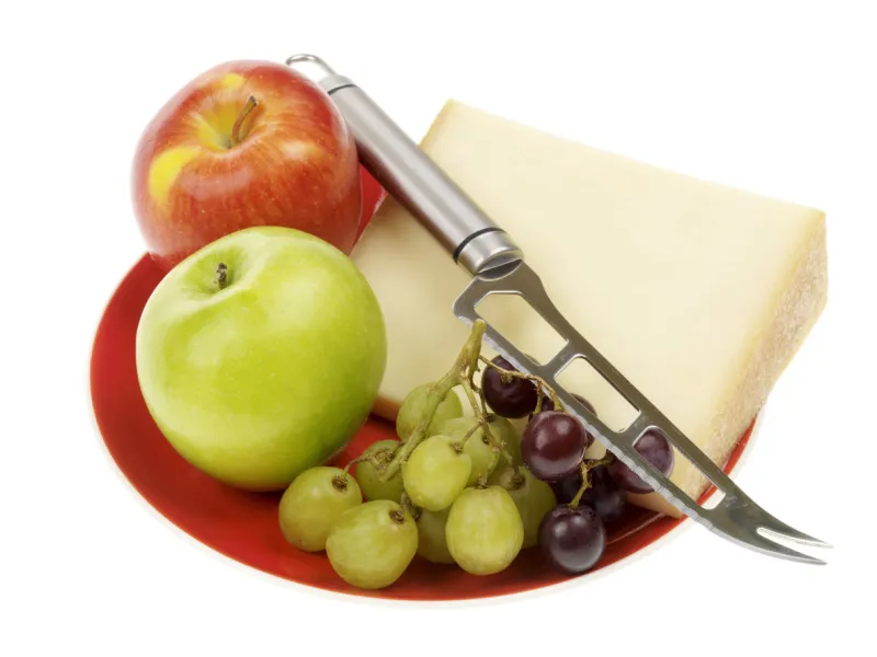 a dslr royalty free image of a plate of beaufort cheese with a selection of fresh ripe juicy fruit including a small bunch of red and green grapes and a single red and green apple with a cheese knife, isolated against a plain white background