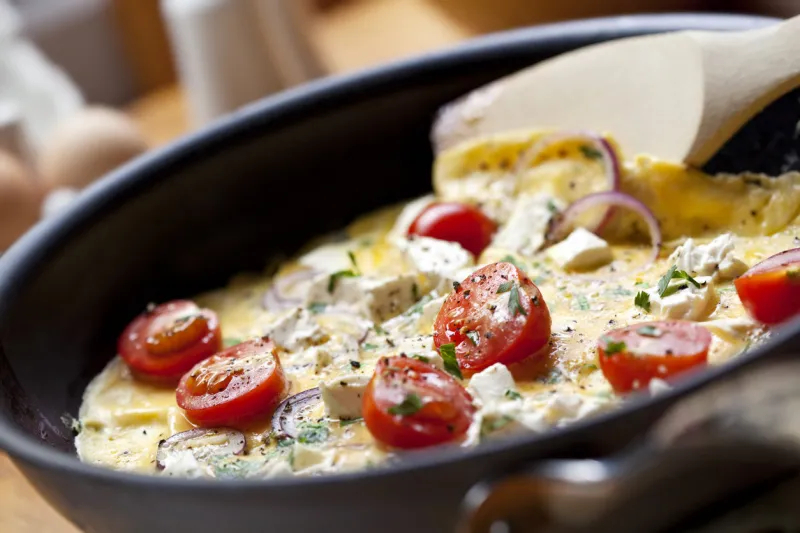 cooking omelet in a pan, ready to serve with cherry tomatoes, red onion, goat's cheese and parsley shallow dof[url=file closeupphp?id=9891133][img]file thumbview approvephp?size=1&amp,id=9891133[ img][ url]