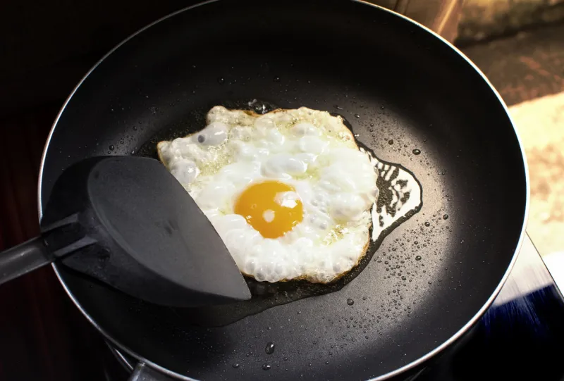 fried sunny side up egg in a black hot pan and plastic spade at kitchen in home