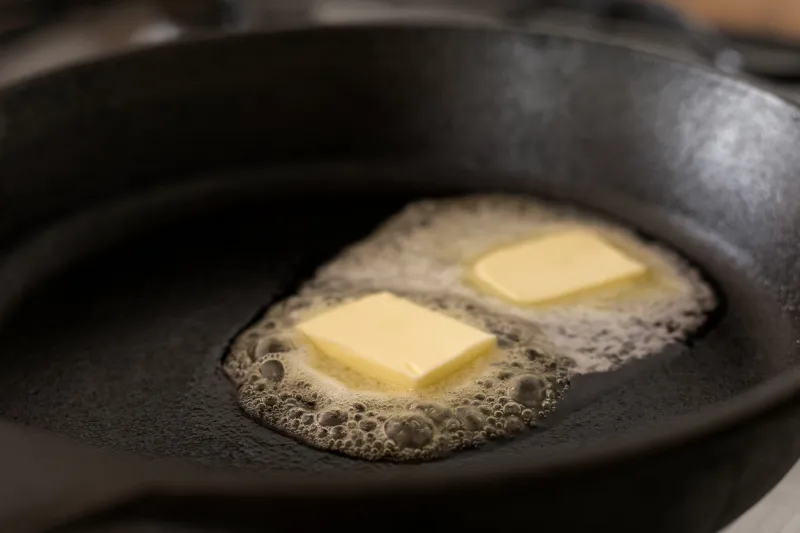 two butter pats melting on a black cast iron frying pan