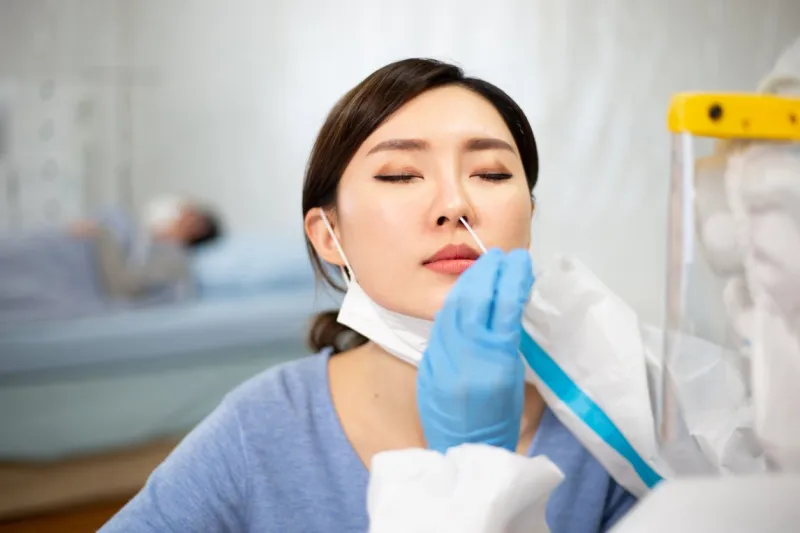 coronavirus test - medical worker taking a swab for corona virus sample from potentially infected woman with the isolation gown or protective suits and surgical face masks