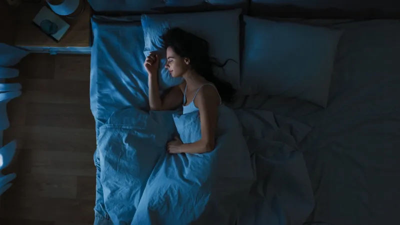 top view of beautiful young woman sleeping cozily on a bed in his bedroom at night blue nightly colors with cold weak lamppost light shining through the window