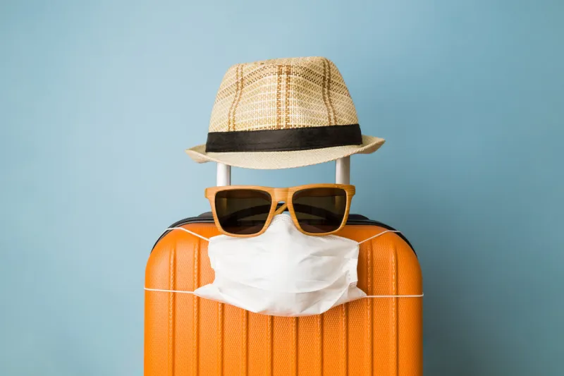 suitcase with hat, sunglasses and protective medical mask on pastel blue background minimal creative coronavirus covid-19 travel concept