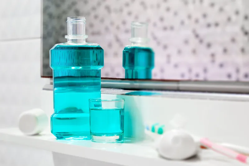 oral cleanser for good oral health, bottle and glass of mouthwash on bath shelf with blurred toothbrush and toothpaste in foreground