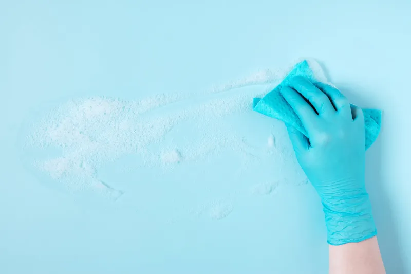 female hand wearing in the blue rubber gloves cleaning surface, blue napkin and foam