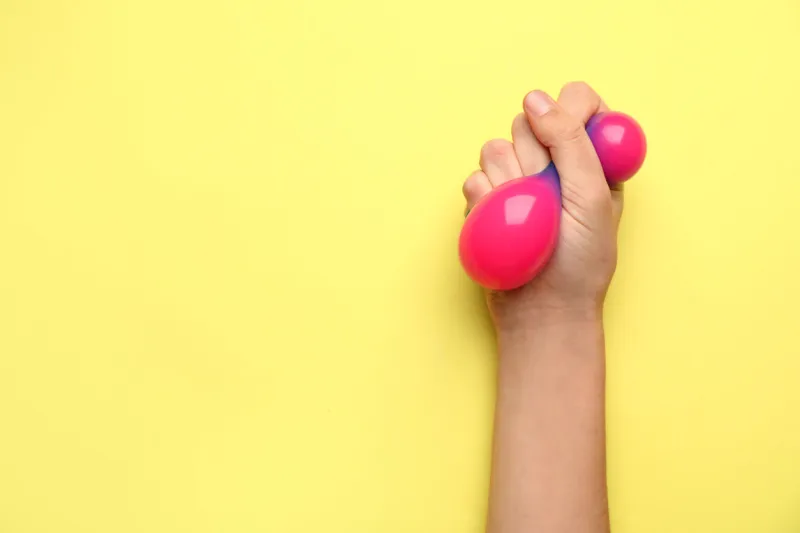 female hand squeezing stress ball on color background