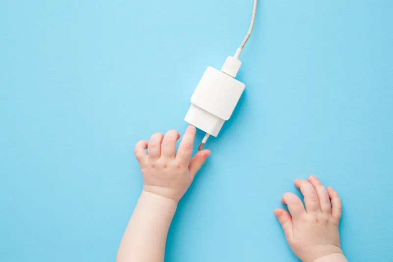 baby hands exploring white charging phone cable with plug on light blue table background pastel color closeup point of view shot top down view