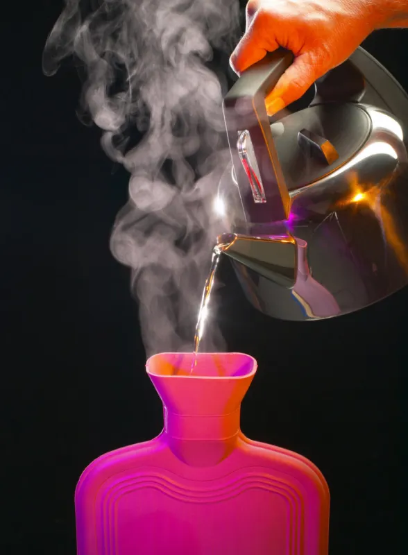 boiling water pouring from kettle into hot water bottle on black background