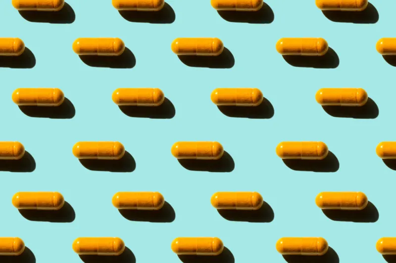 pattern of orange curcumin turmeric pills with shadow on blue background