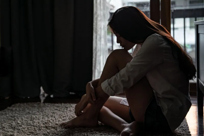 selective focus loneliness young asian woman sitting on bedroom floor near the balcony depression sadness breaking up asian teenage girl sitting alone hugging knees closing eyes and thinking