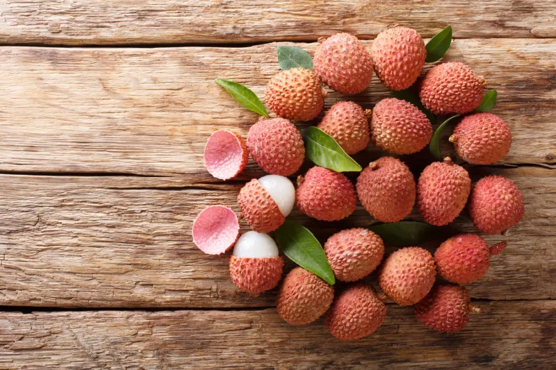 ripe lychee fruits with green leaves close-up on wooden background horizontal top view from above
