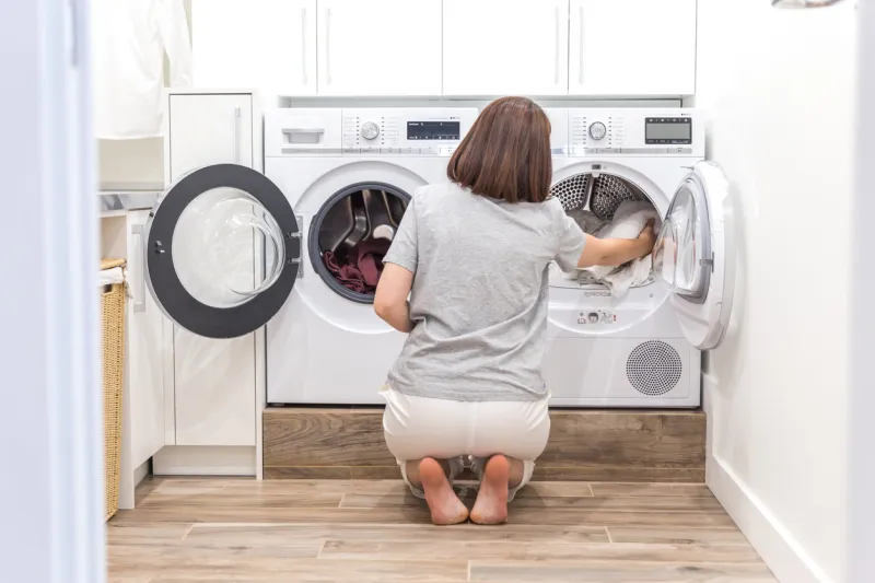 woman loading dirty clothes in washing machine for washing in modern utility room