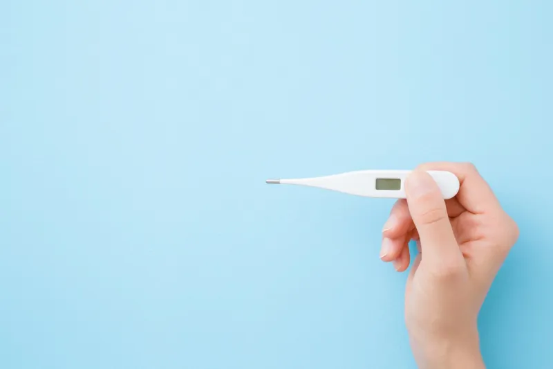 young woman hands holding white digital thermometer on pastel blue background fever and healthcare concept closeup point of view shot empty place for text top down view