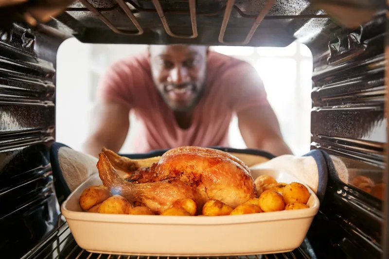view looking out from inside oven as man cooks sunday roast chicken dinner