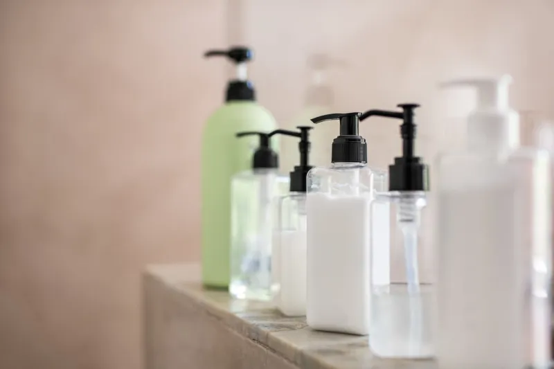 dispenser bottles in a row kept on rack in bathroom close up of multiple shampoo, soap and body lotion bottles on marble at spa bottle of soap and liquid in bathroom