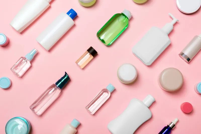 top view of different cosmetic bottles and container for cosmetics on pink background flat lay composition with copy space