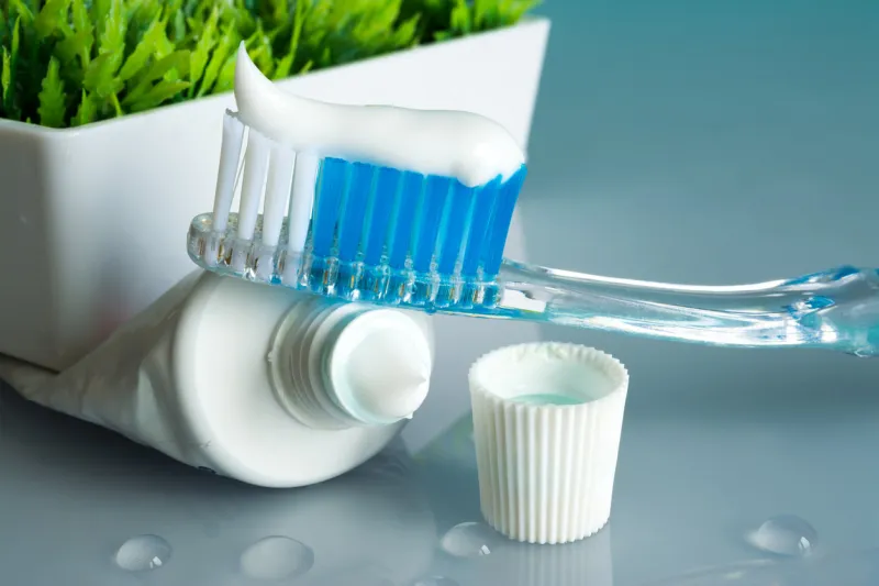 new toothbrush with toothpaste close-up in the bathroom on a mirror table with water drops on a blue background in the sunlight