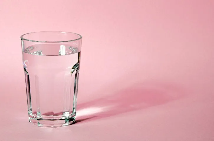 glass beaker from which padajet sharp shadow, stands on a pink background empty space for text