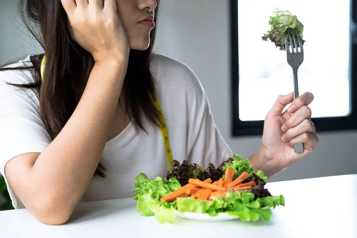 unhappy asian women is on dieting time looking at vegetable on the fork